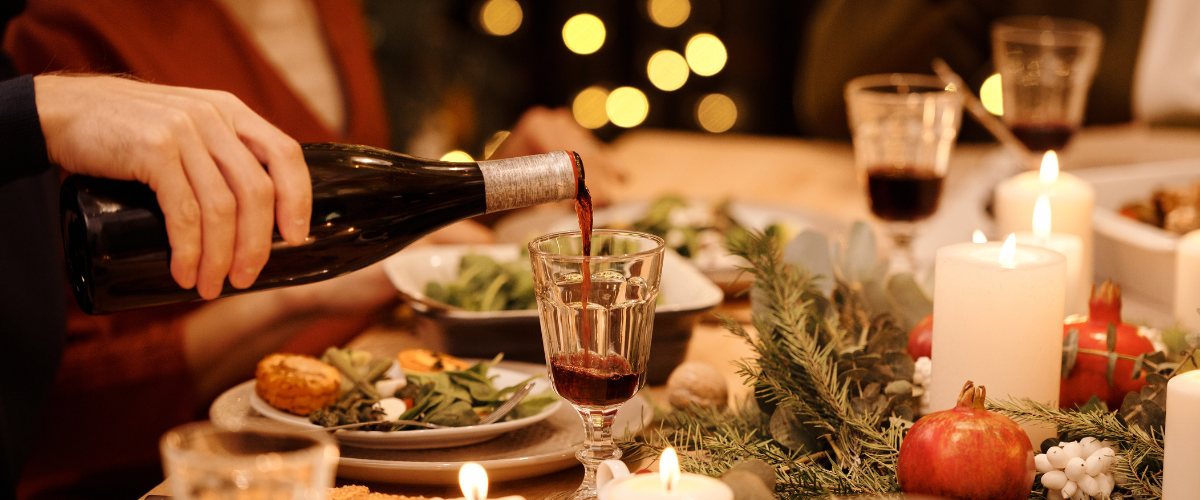 A fuzzy view of a christmas dinner table, a man's hand pouring red wine into a crystal goblet